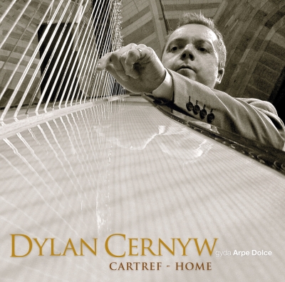 A suited man leans over a harp, reaching among its diagonal strings, with gold lettering across the pale soundboard.