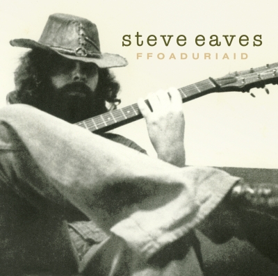 A shadow-faced, bearded figure in a broad hat holds a guitar while a bent leg in light trousers fills the foreground.