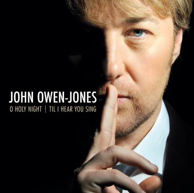A close-up portrait of a man holding one finger to his lips, with white and pale-gold lettering on the black space beside him.