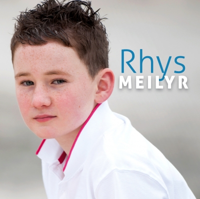 A young person with tousled dark hair and a white shirt looks towards the viewer beside the blue name “Rhys” and white “MEILYR”.